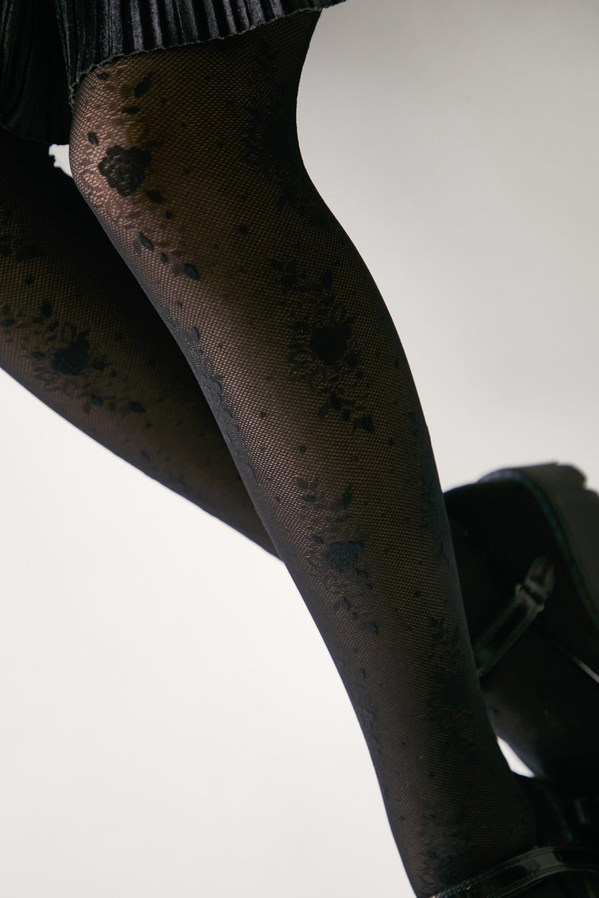 Black patterned tights featuring a delicate floral lace design worn with dark platform shoes against a plain white background.