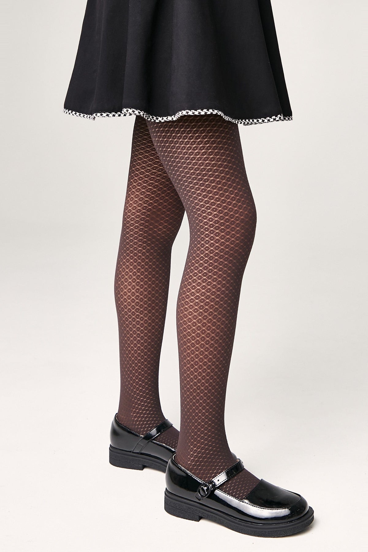 Brown tights with a fine geometric honeycomb pattern worn with a black skirt and glossy black Mary Jane shoes.