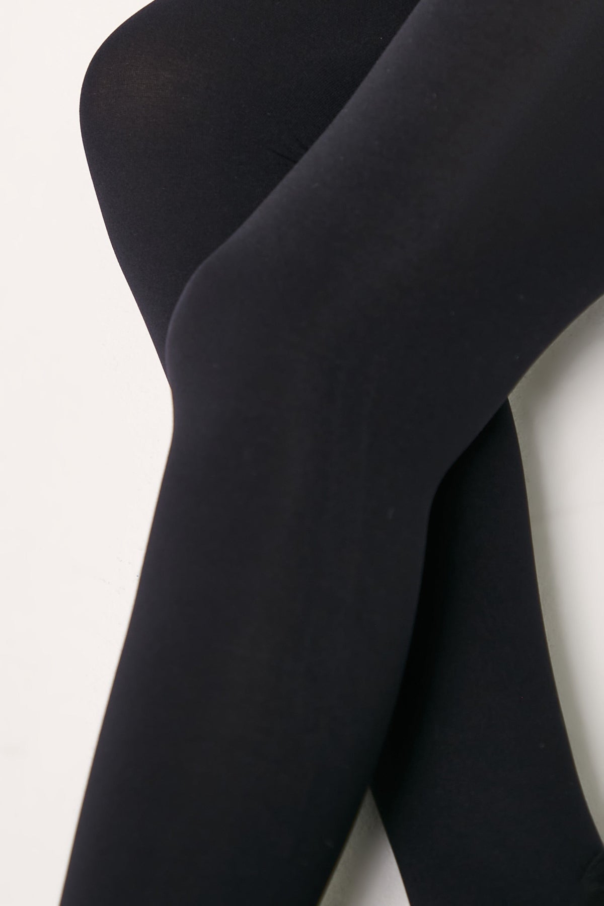 A close-up view of legs wearing opaque black tights against a plain white background.