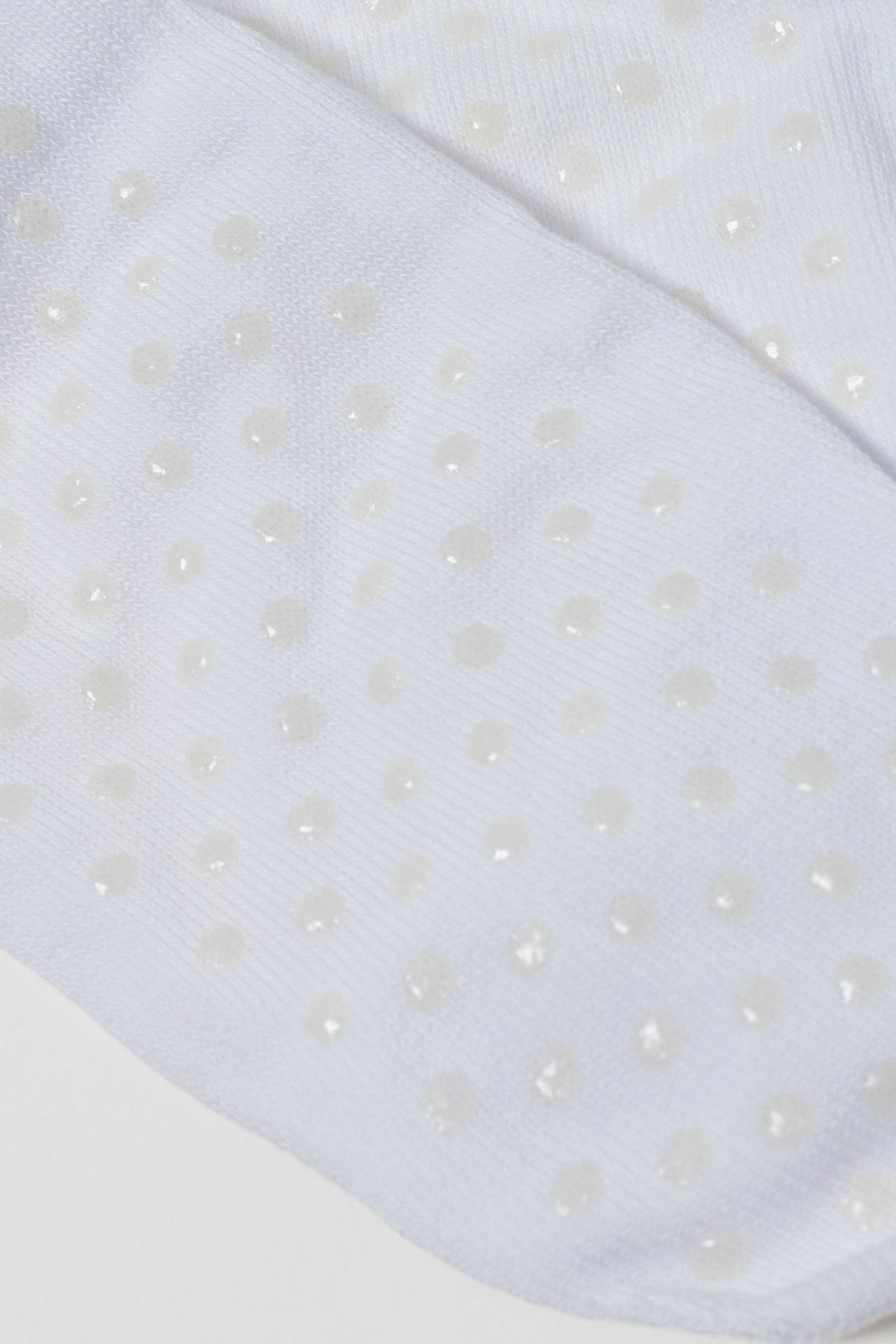A close-up view of white socks featuring a repeating pattern of small, translucent, circular grip dots on the fabric surface.
