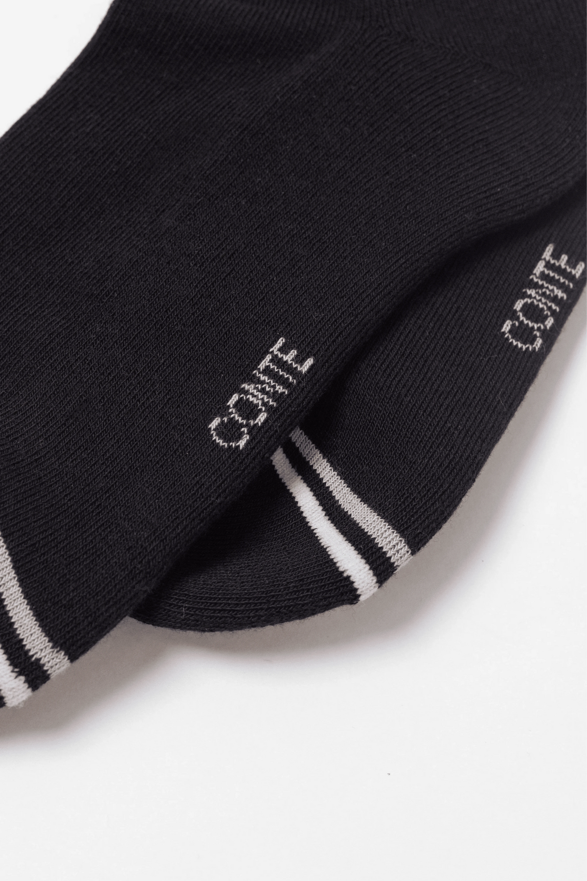 A pair of black ankle socks featuring the word CONTE in light pink lettering above a thin pink and white striped band on a white background.