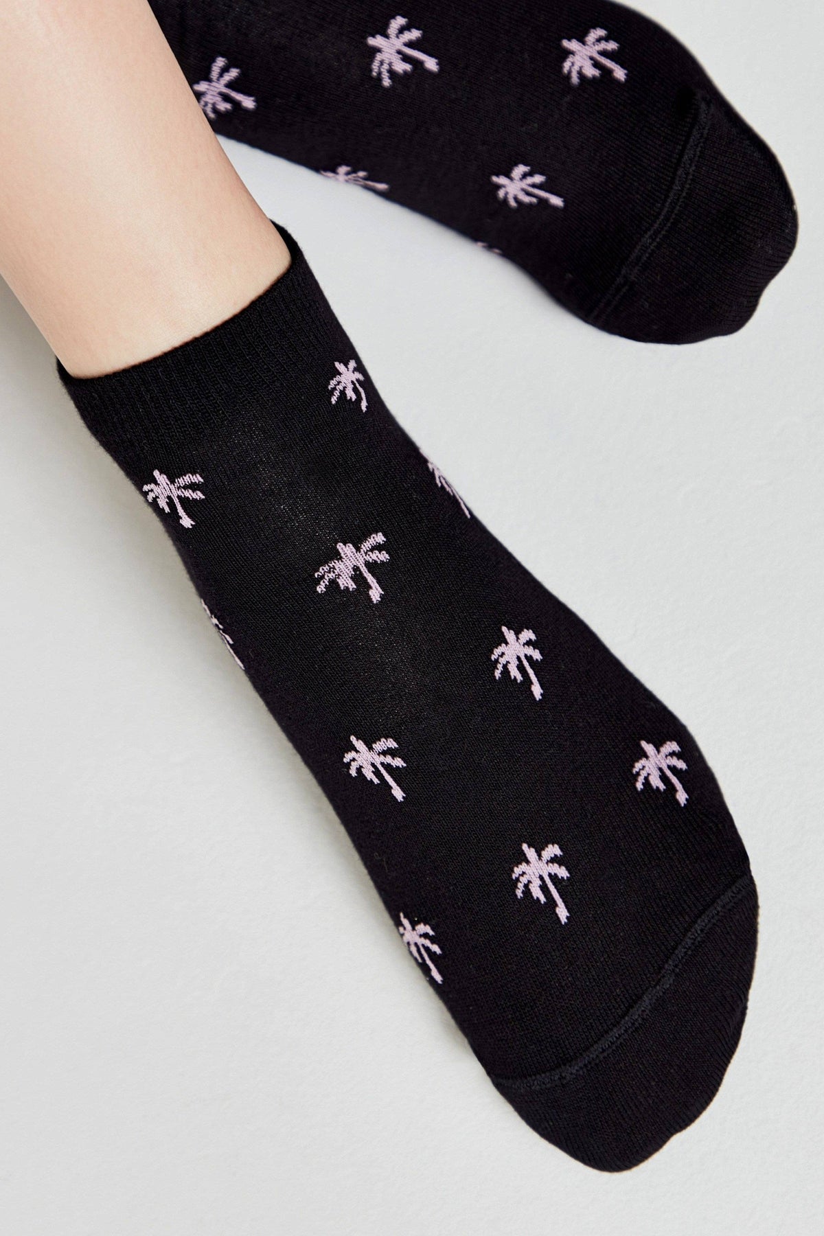 A pair of black ankle socks featuring a repeated small light purple palm tree pattern.