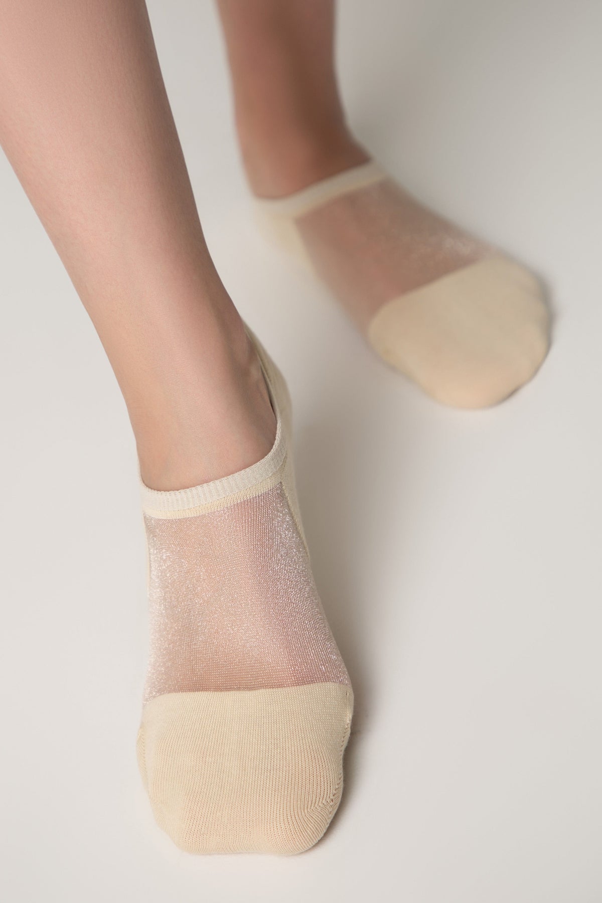 A pair of sheer beige low-cut socks worn on feet against a plain white background.