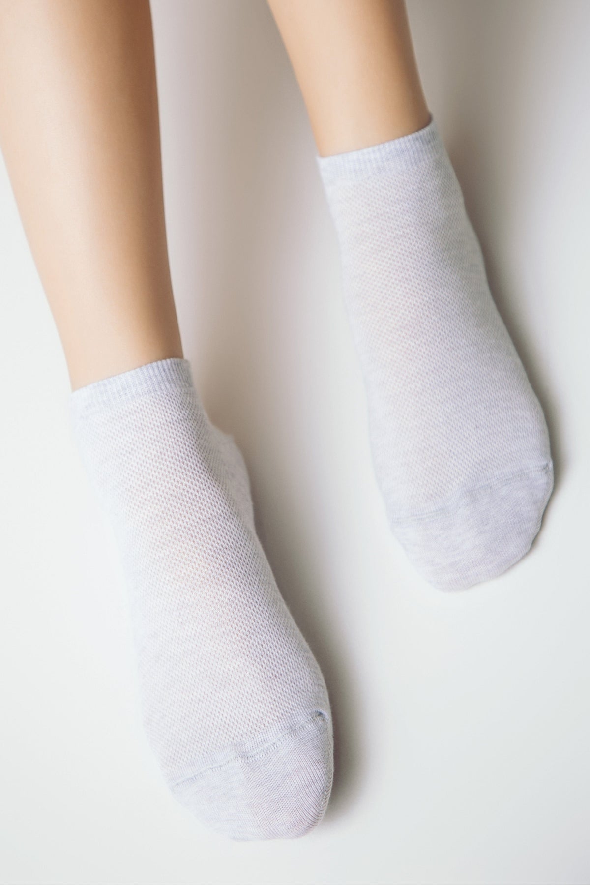 A pair of pale grey ankle socks with a fine mesh knit texture worn on a person's feet against a plain white background.