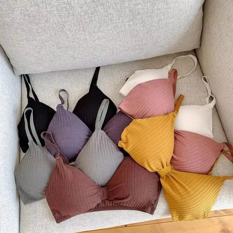 A variety of ribbed triangle-style bralettes in assorted colors including black, grey, purple, pink, white, and mustard yellow arranged on a light-colored sofa.