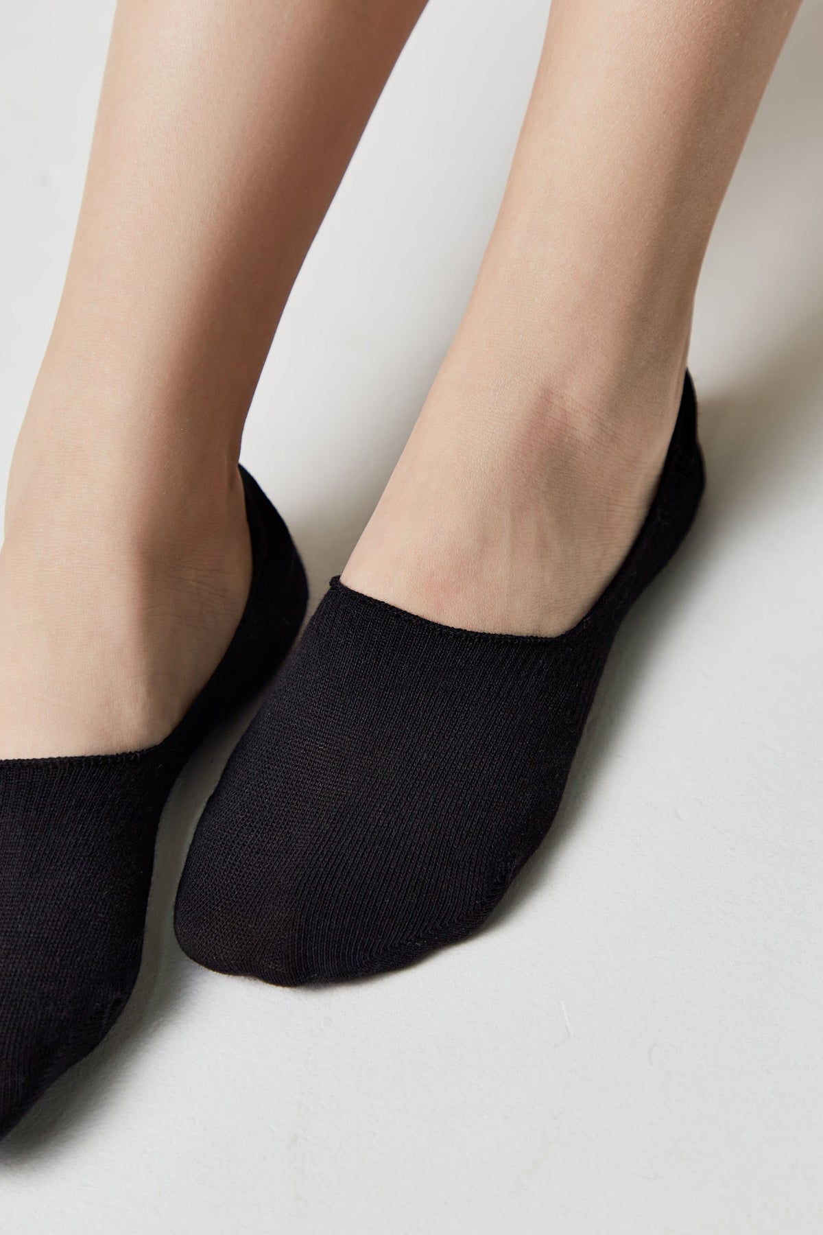 A pair of black no-show socks worn on a person's feet against a plain white background.