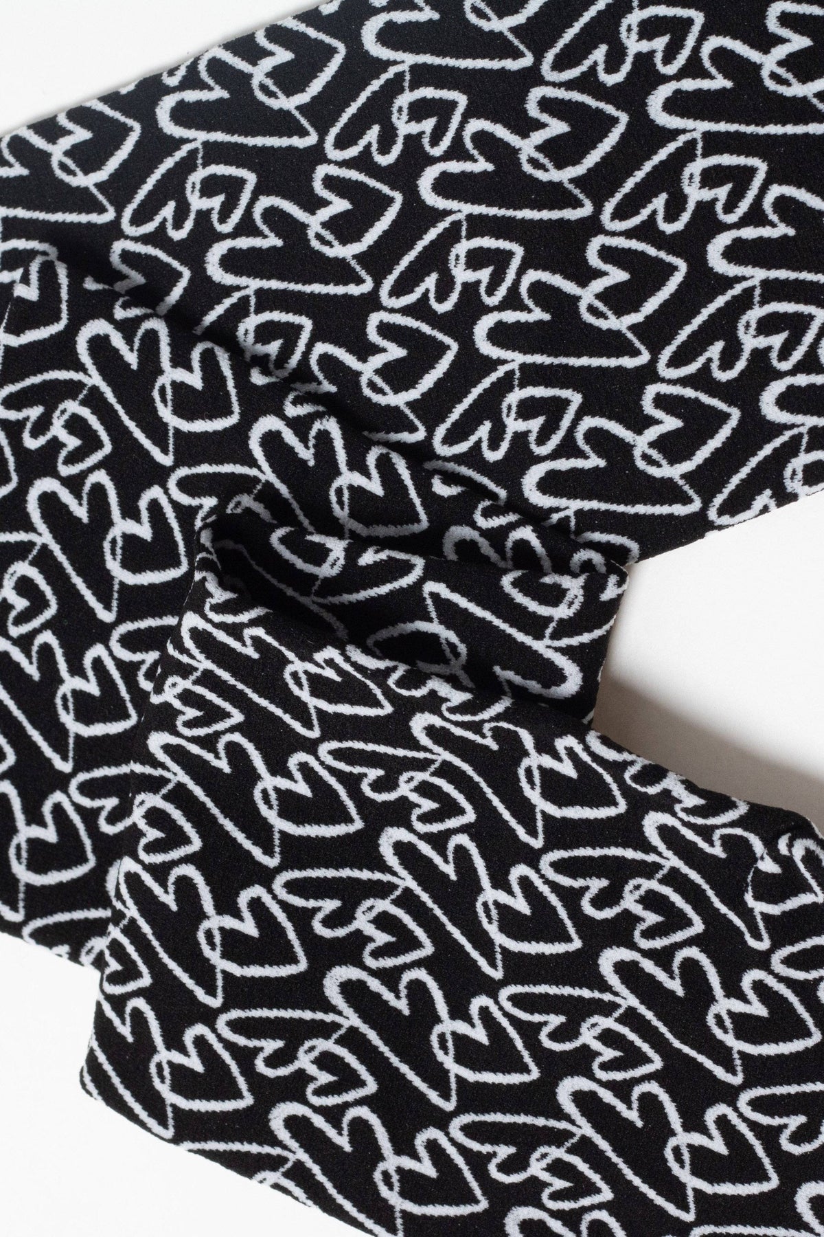 A black fabric with a repeating white hand-drawn heart pattern folded against a plain white background.