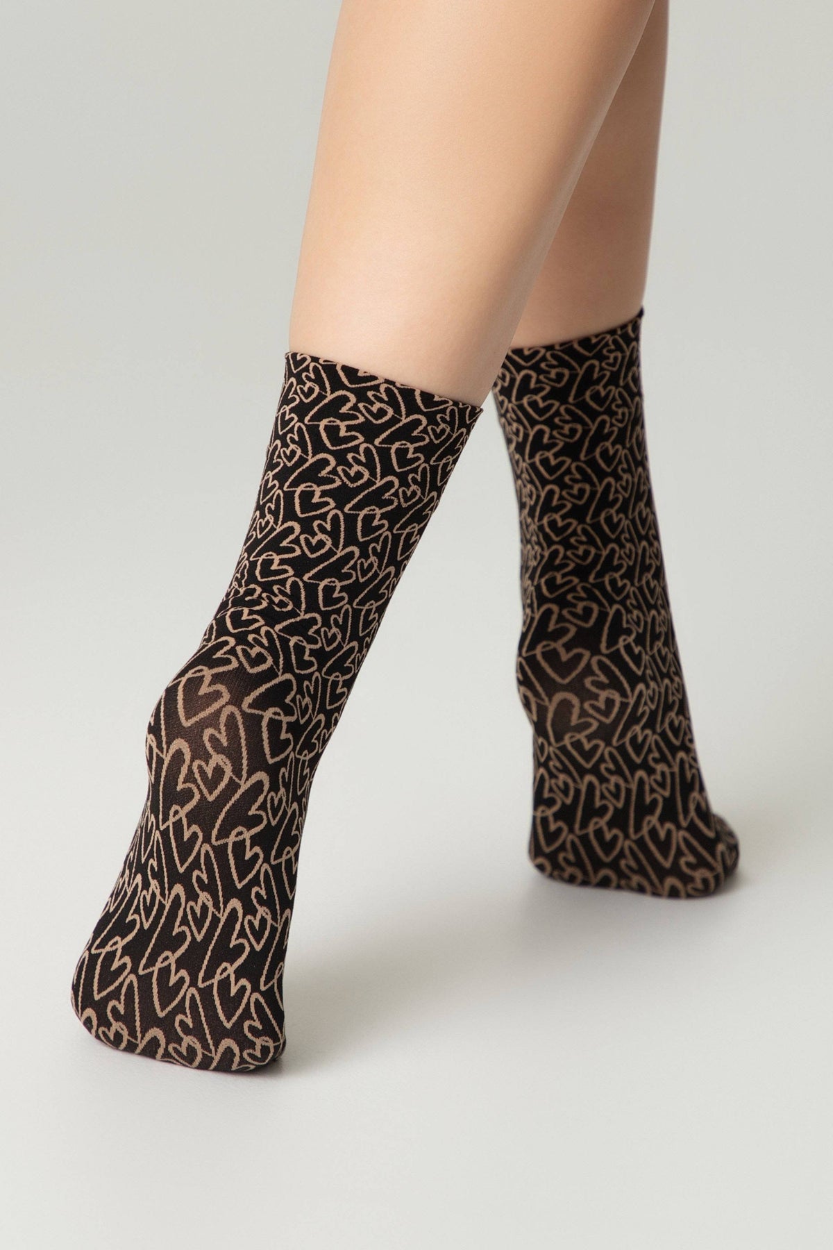 Ankle socks featuring a brown and black heart pattern worn on a person's legs against a plain light gray background.