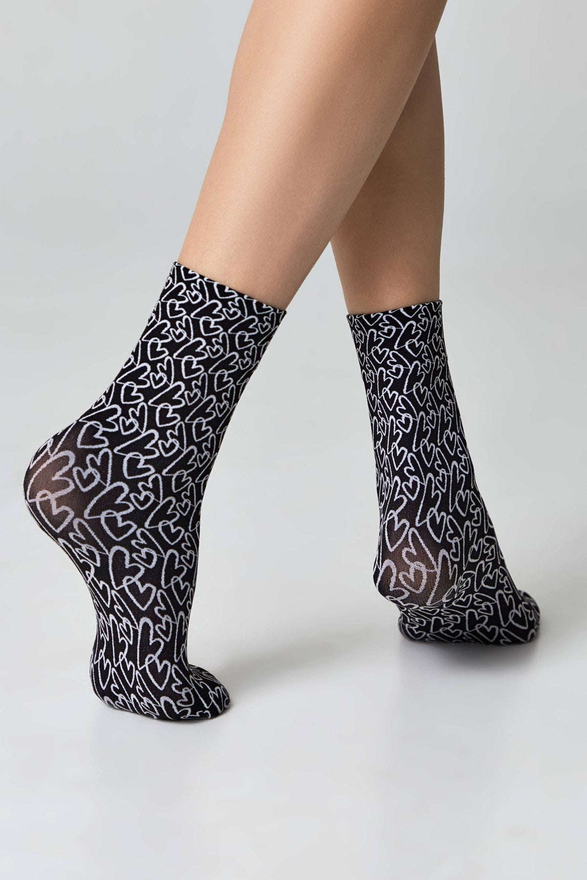 A pair of black socks patterned with white outlined heart shapes, worn on a person's feet against a plain white background.