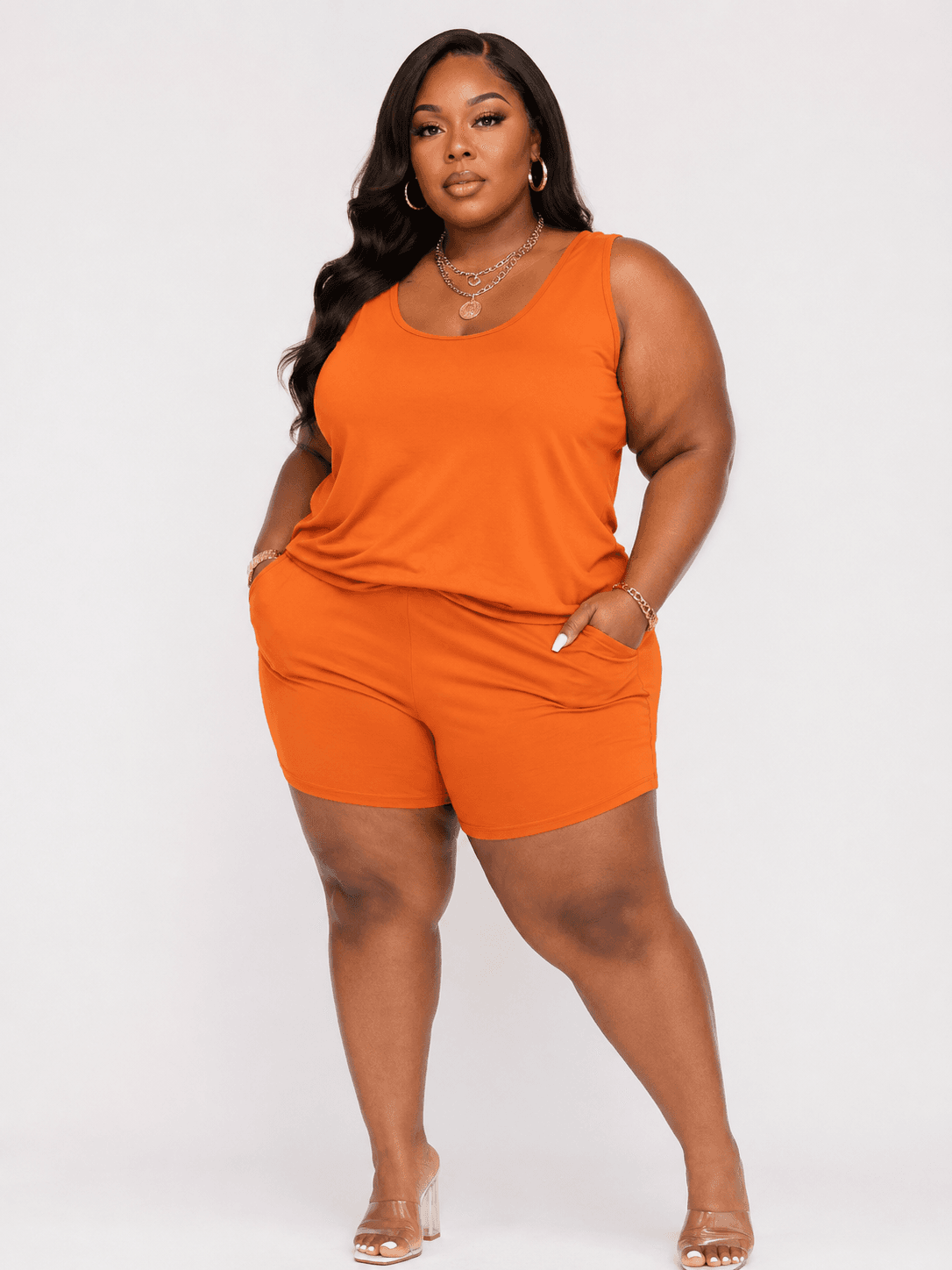 A woman wearing a matching set consisting of an orange sleeveless tank top and loose shorts with side pockets.