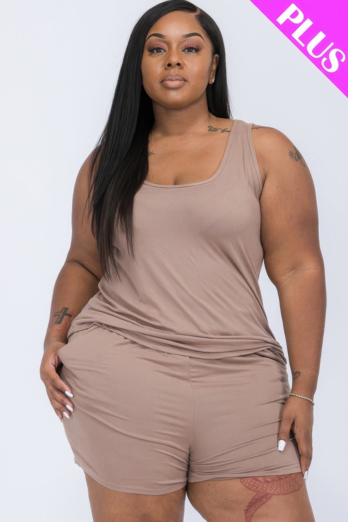 A woman wears a taupe-colored tank top and matching shorts set against a white studio background.
