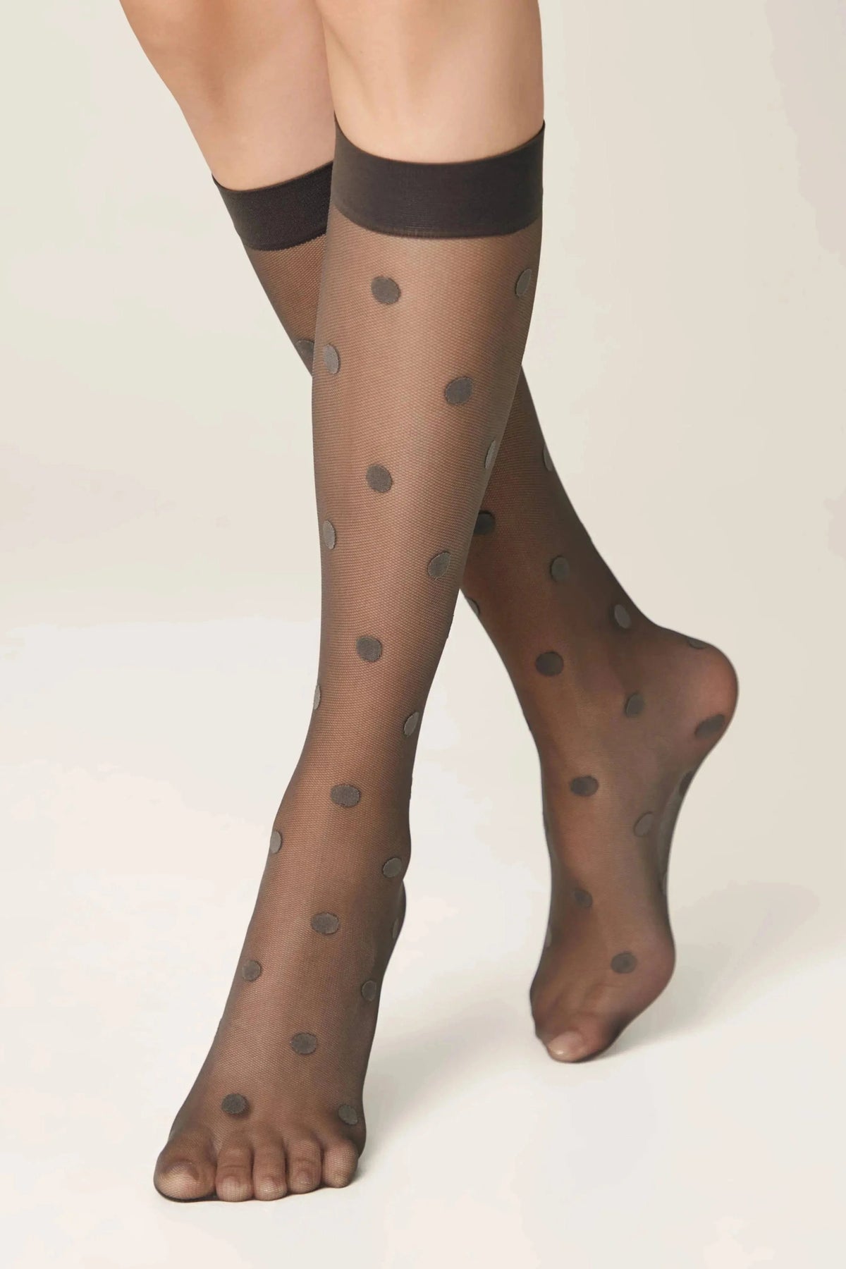 Sheer black knee-high stockings featuring a repeating dark polka dot pattern worn on a person's legs against a plain light background.