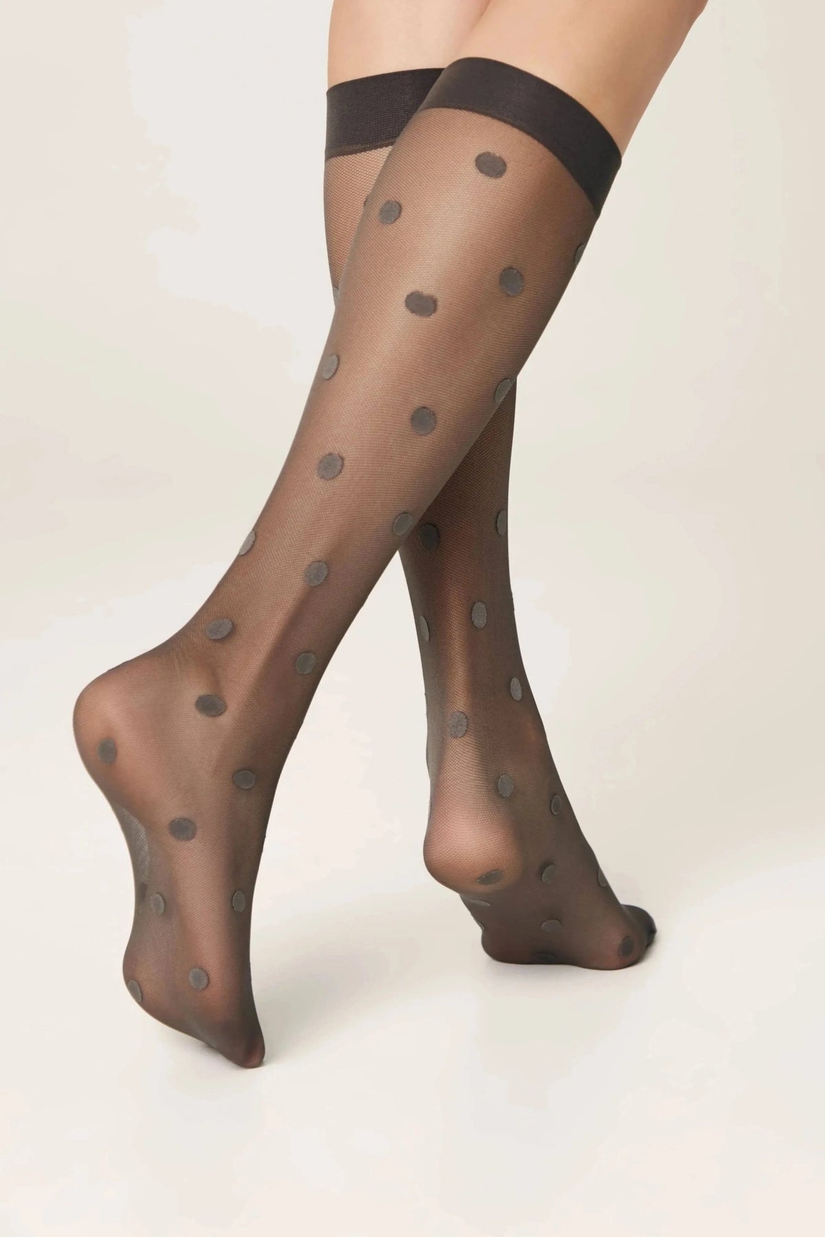 Sheer black knee-high stockings with a small circular polka dot pattern worn on a pair of legs against a plain light background.