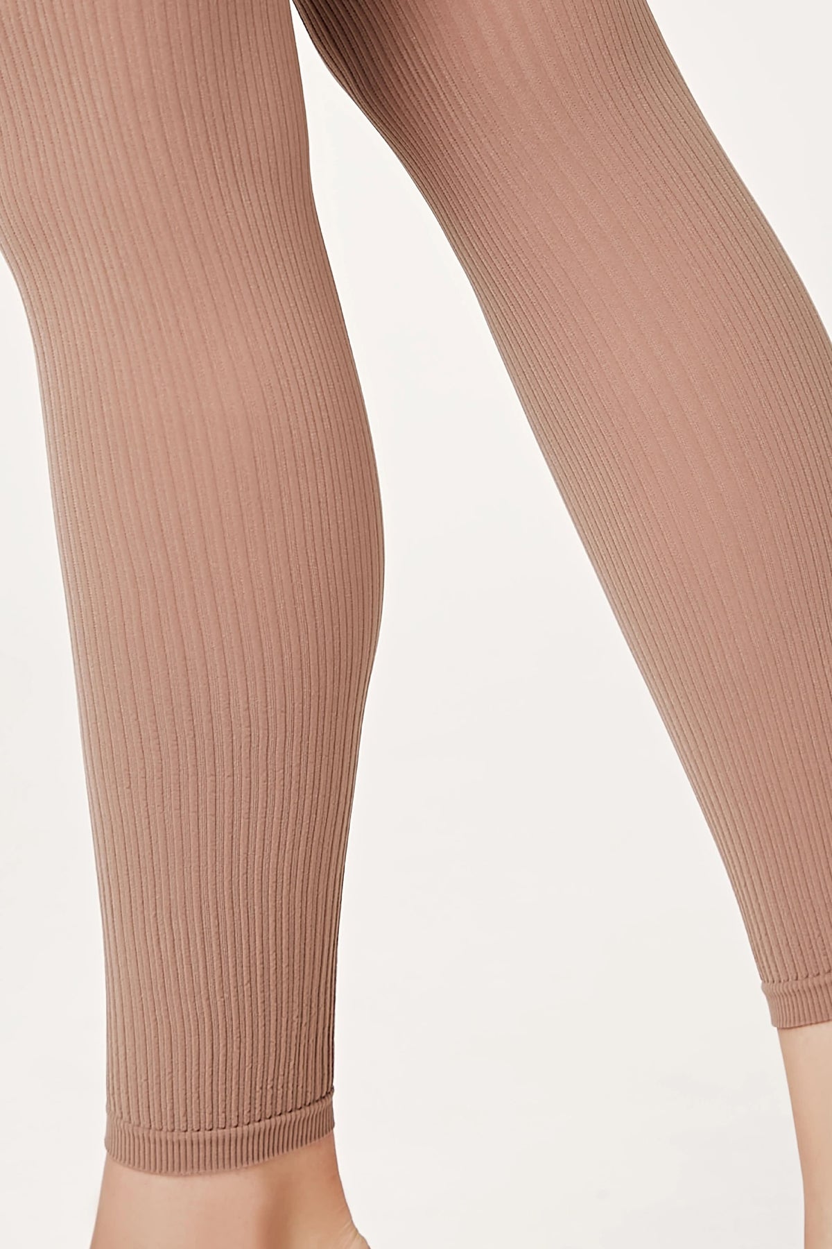 A close-up view of ribbed, tan-colored leggings worn on legs against a plain white background.