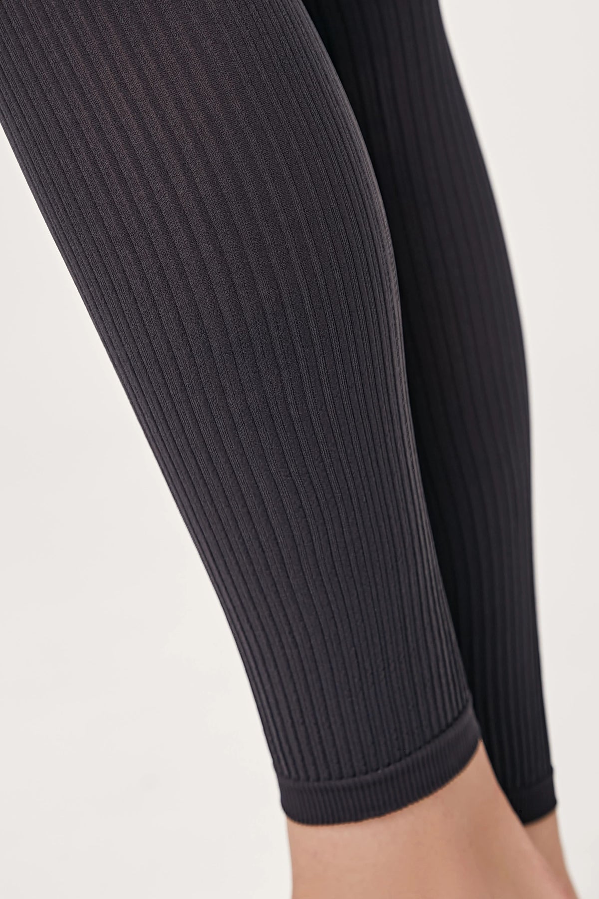 Close-up of a pair of charcoal grey ribbed leggings worn on the lower legs.
