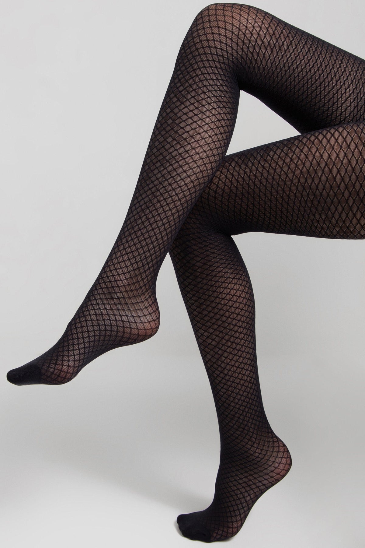 Black diamond-patterned fishnet tights worn on legs against a plain grey background.