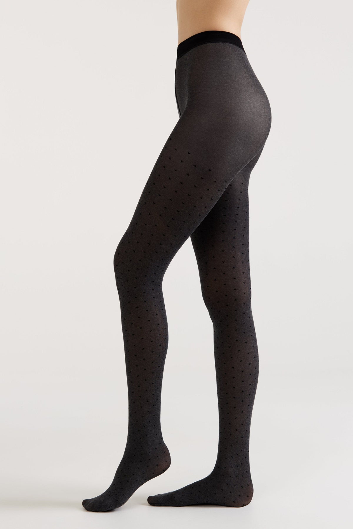 A side view of a person wearing dark grey tights featuring a subtle, repeating heart-shaped pattern.