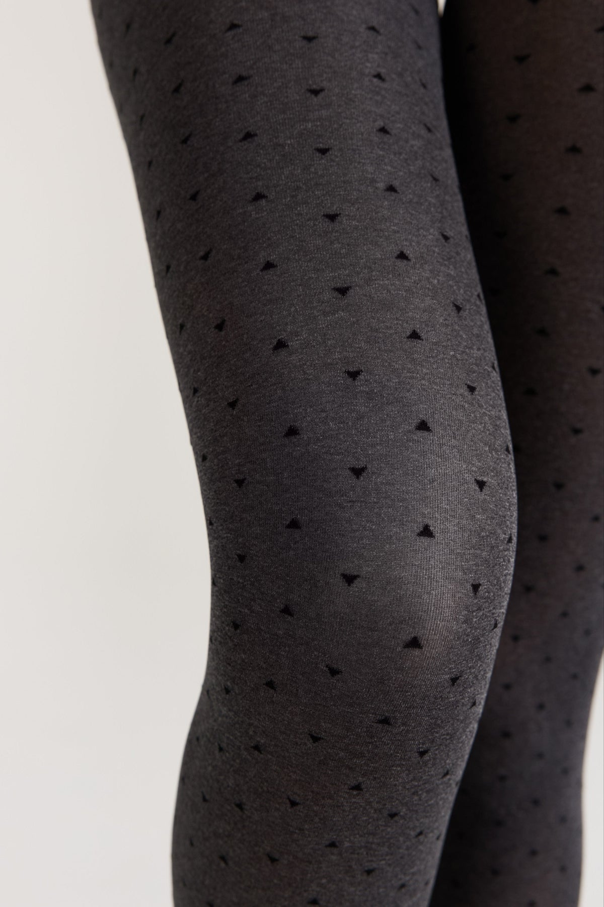 A close-up of dark grey patterned tights featuring a repeating print of small black triangles worn on a pair of legs.