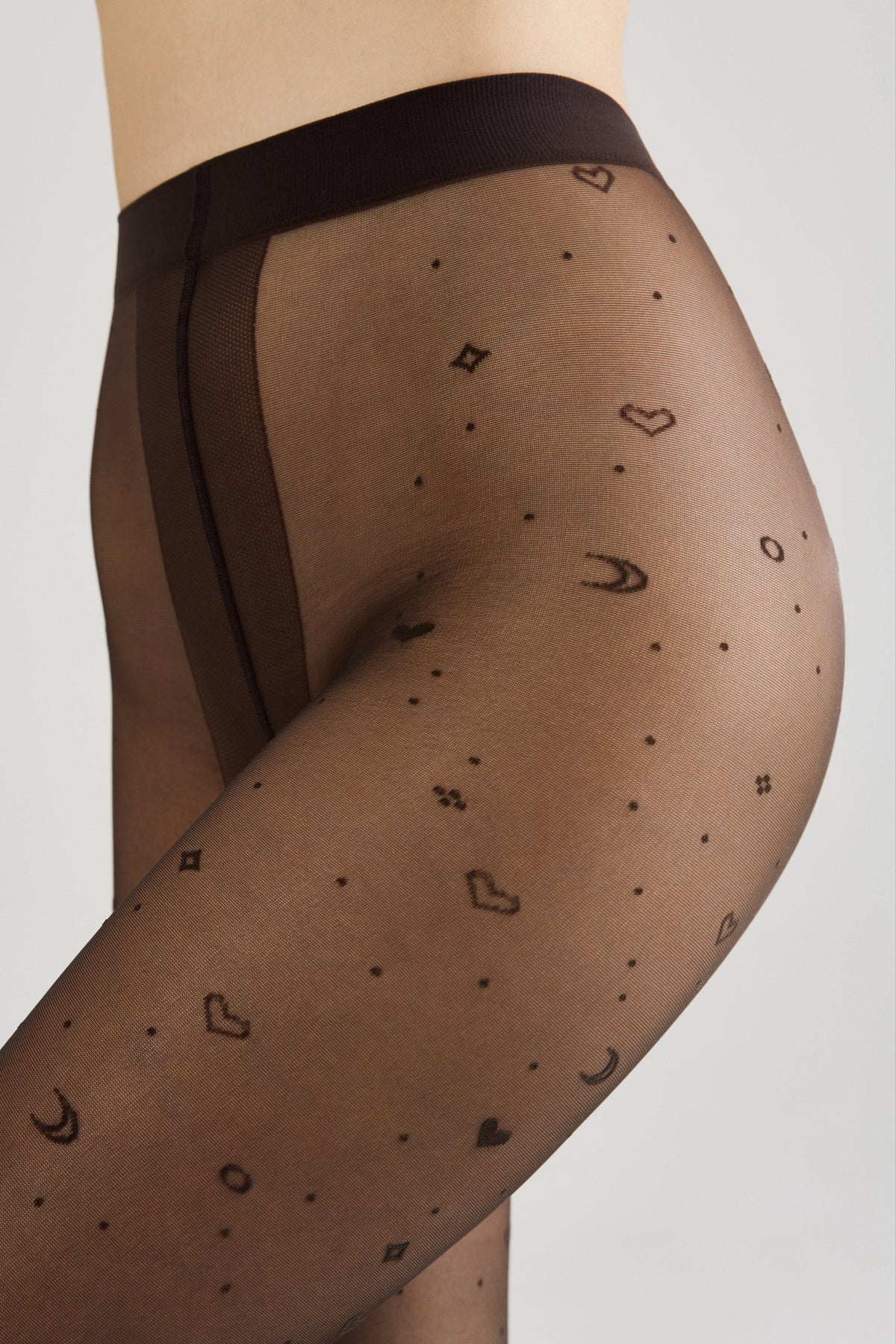 Sheer black pantyhose patterned with small scattered hearts, stars, crescents, and dots worn on a person's torso and upper thigh against a neutral background.