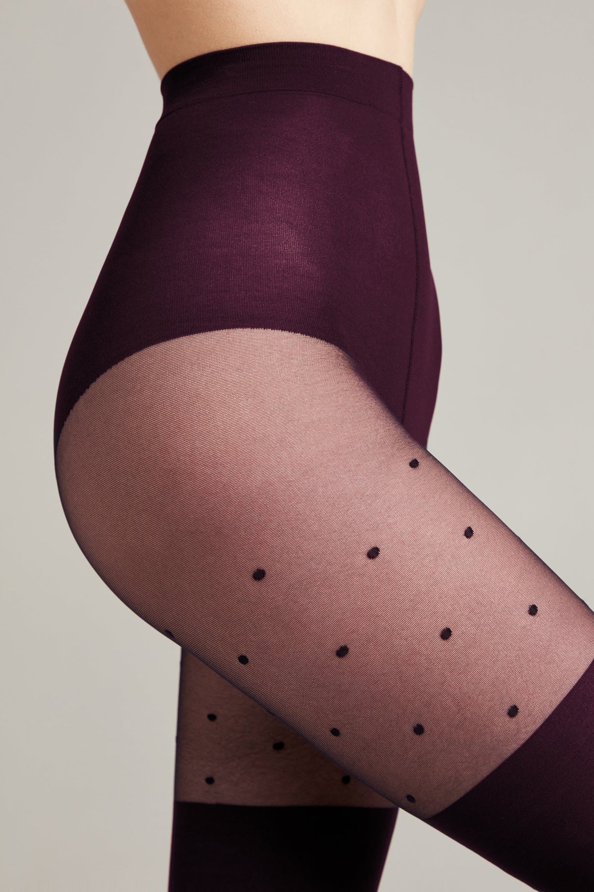 A pair of dark purple opaque tights featuring a sheer section on the thigh decorated with small black polka dots.