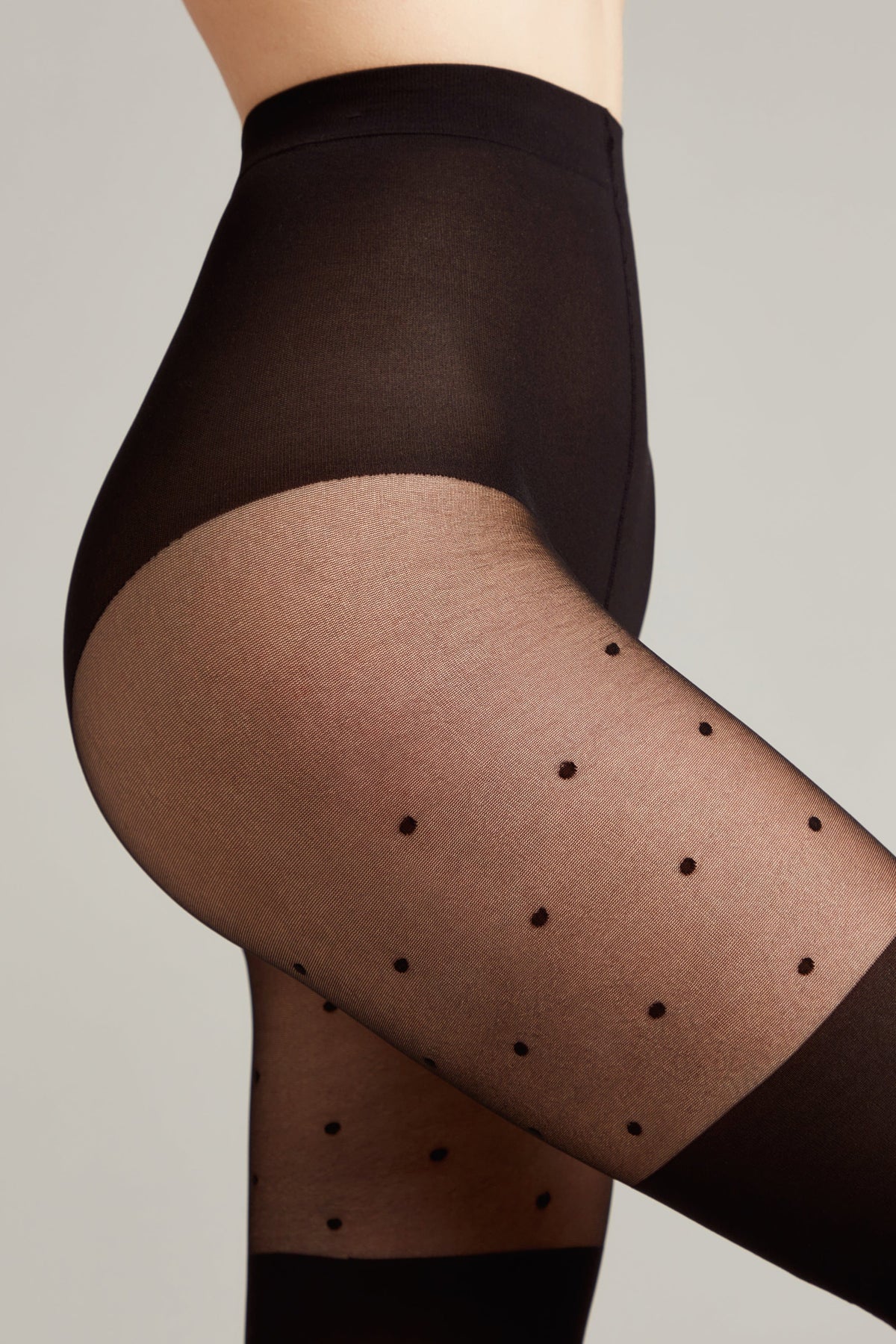 Black sheer pantyhose with a polka dot pattern and an opaque high-waist band worn on a person's side profile.