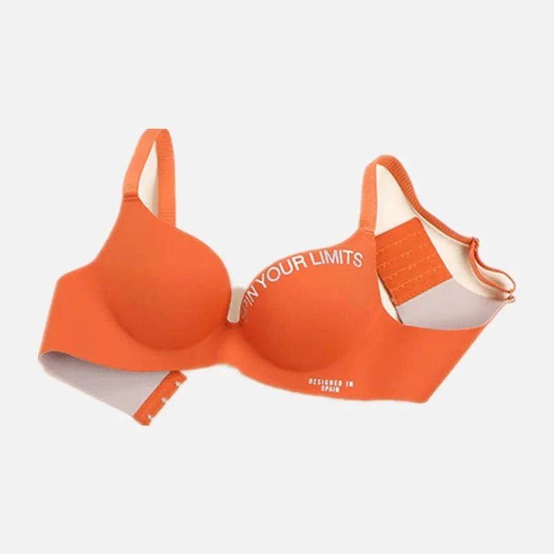 An orange wireless bra featuring white text that reads "SPIN YOUR LIMITS" on the cup and "DESIGNED IN SPAIN" on the band, shown against a light background.