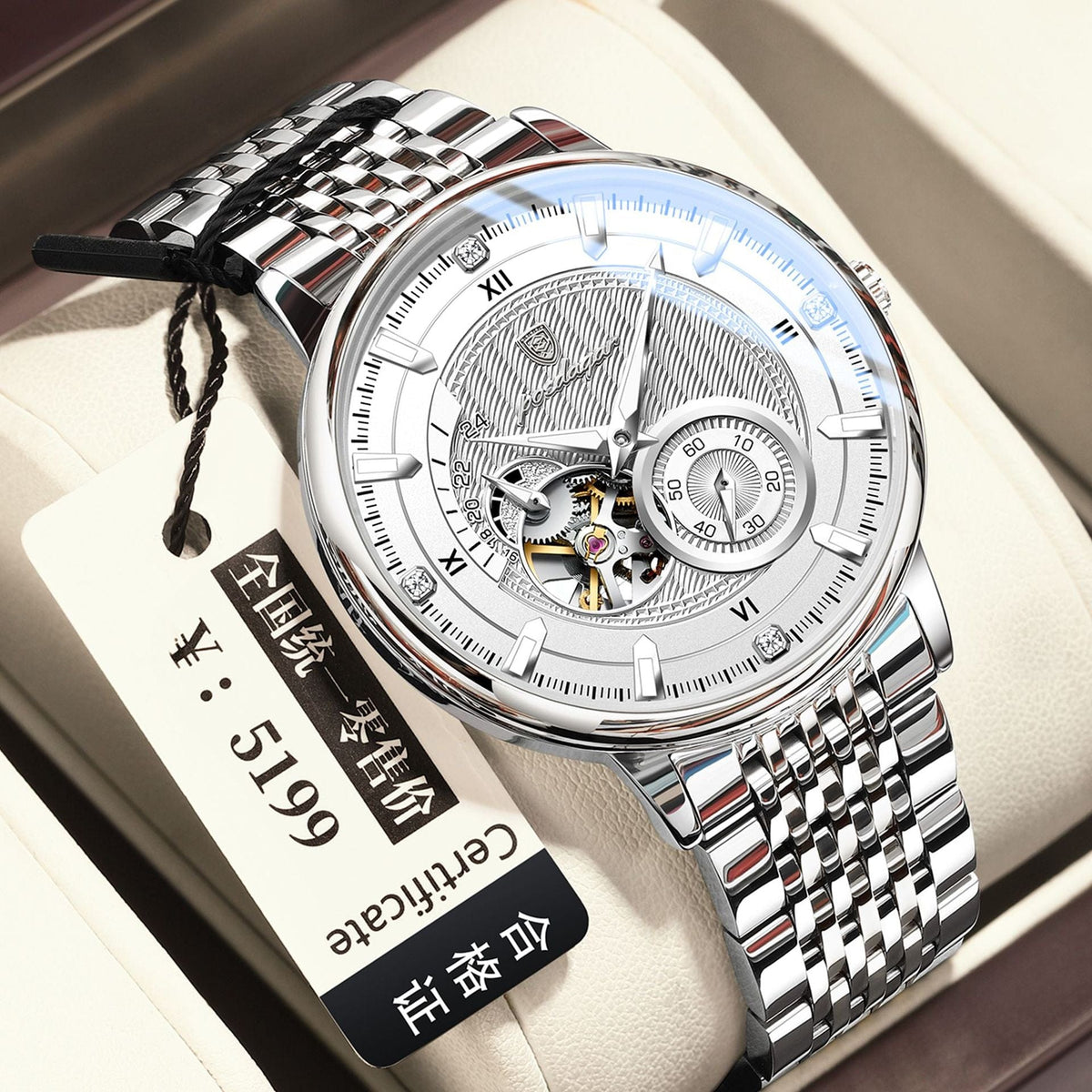 A silver-tone automatic wristwatch with a metallic multi-link bracelet is displayed inside a cushioned presentation box alongside a price tag.