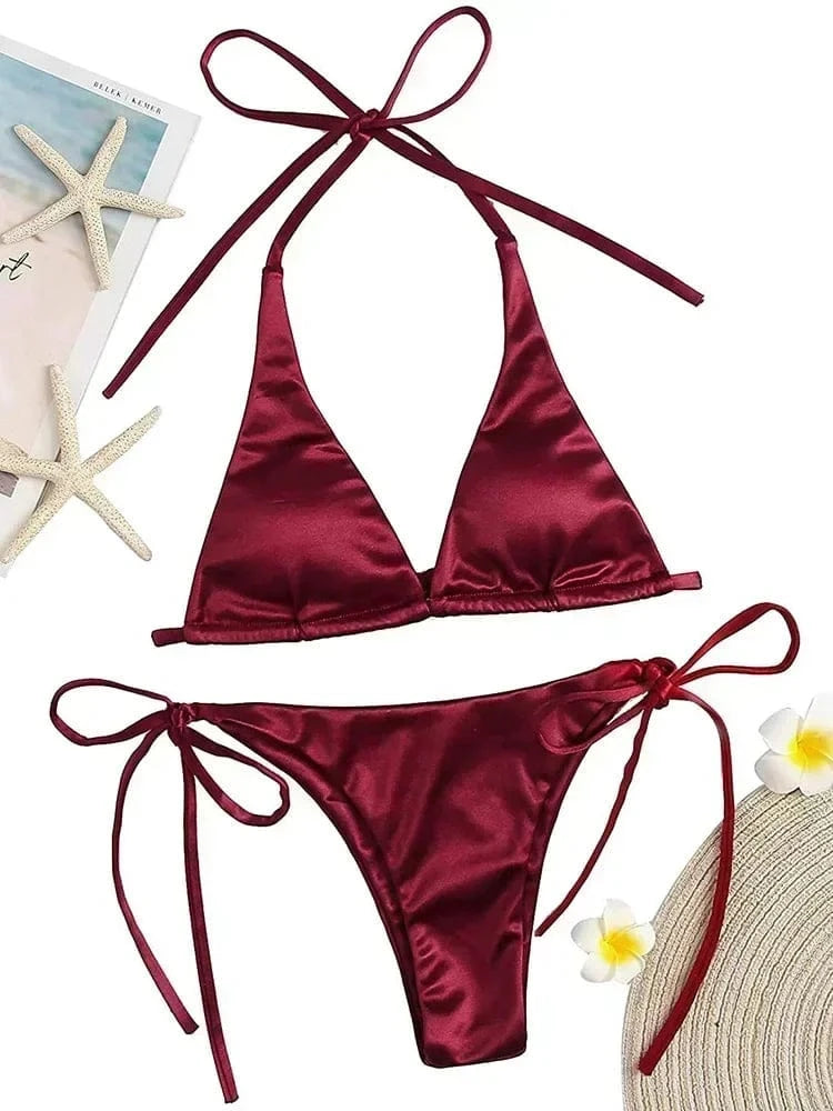 A maroon satin bikini set featuring a triangle top and side-tie bottoms, displayed alongside two starfish and two small white flowers.