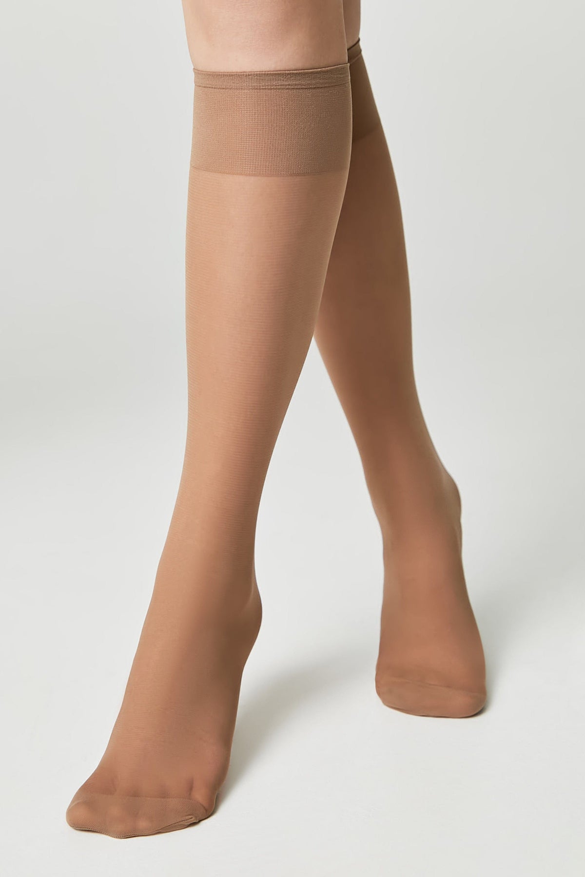 A pair of sheer tan knee-high stockings worn on legs against a plain white background.