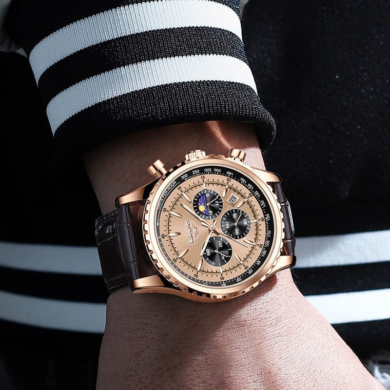 A gold-toned chronograph wristwatch with a light gold dial, three sub-dials, a moon phase display, and a dark brown leather strap worn on a wrist.