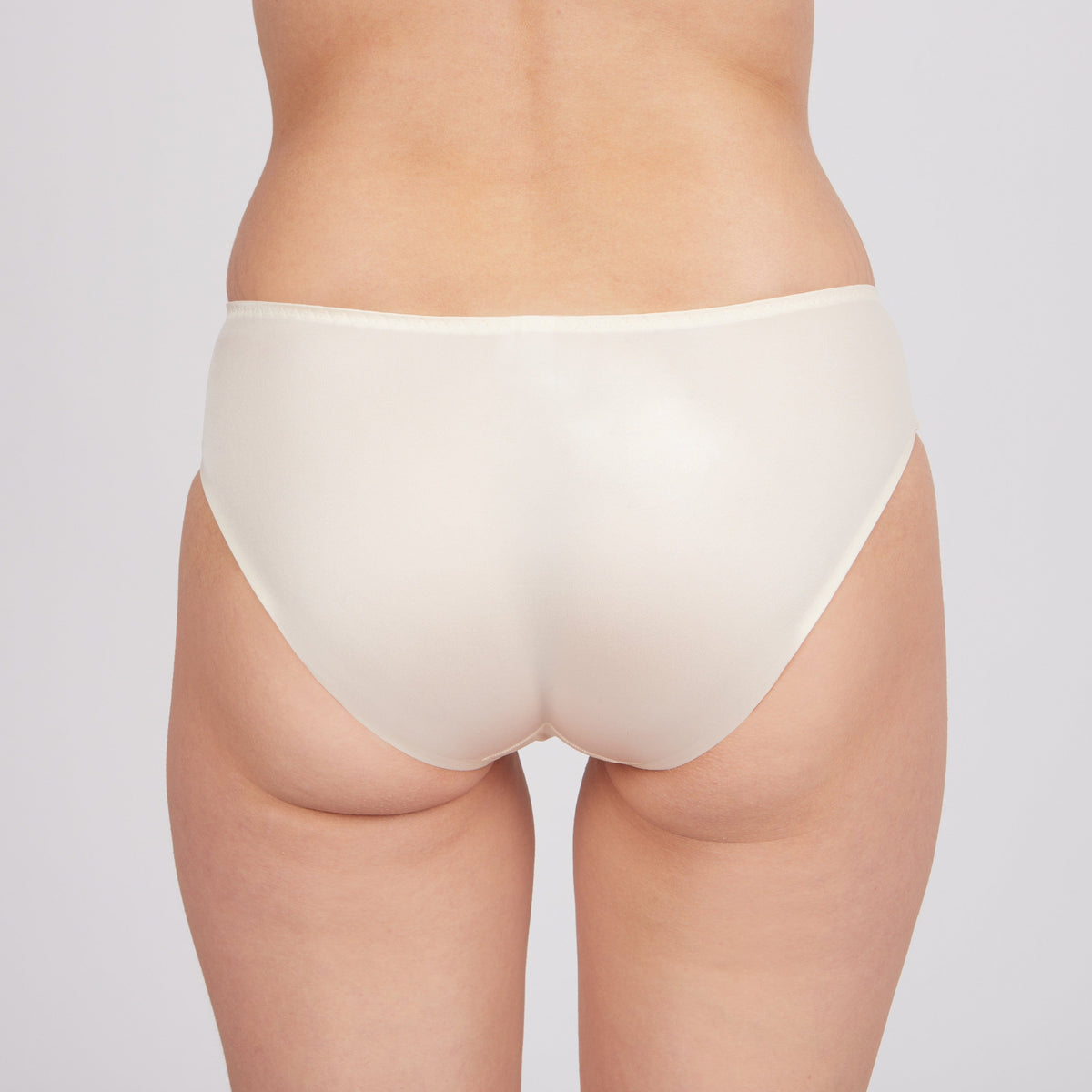A back view of a person wearing solid light beige, full-coverage briefs against a plain grey background.