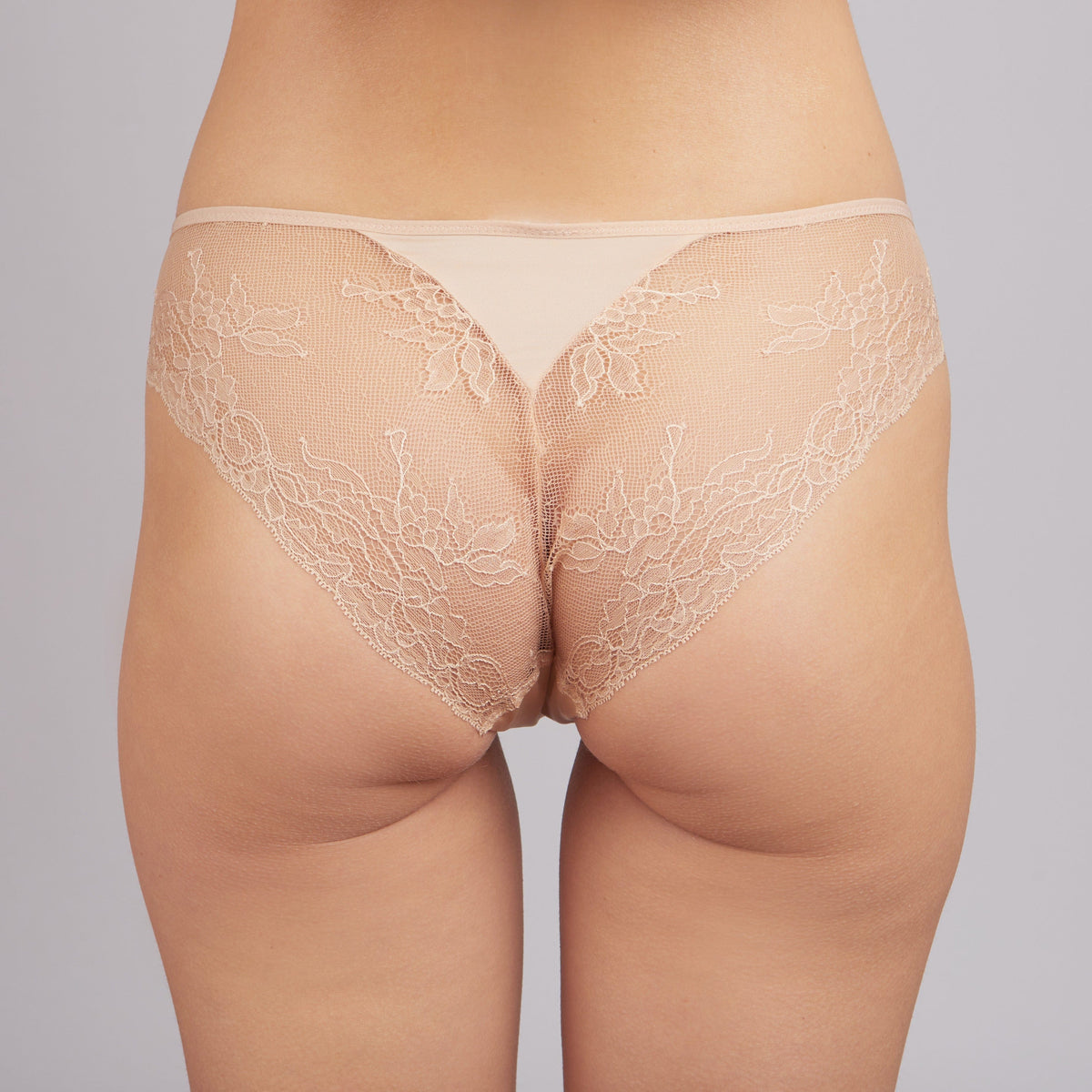 Beige lace panties with a smooth fabric waistband worn from behind on a person.