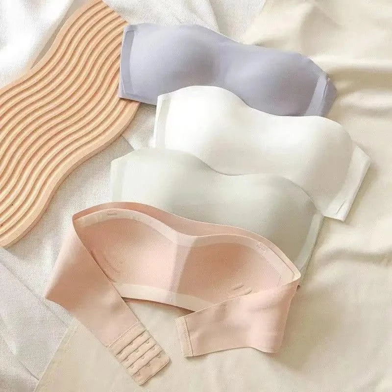 Three strapless bras in light purple, white, and beige are arranged on a soft fabric surface next to a wavy, light-toned wooden board.