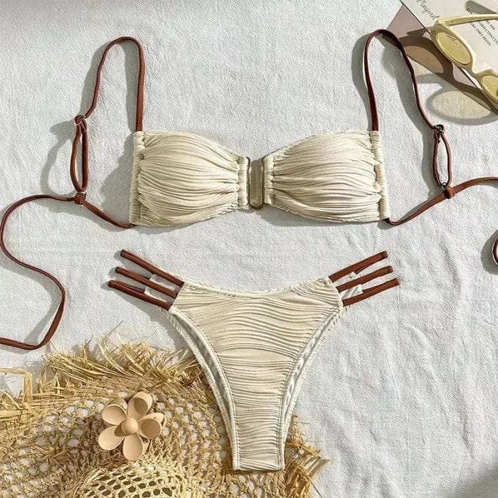 A beige two-piece bikini featuring a textured, ruched bandeau top with a central gold-tone clasp and matching high-cut bottoms with triple-strap hip detailing and contrasting brown ties.