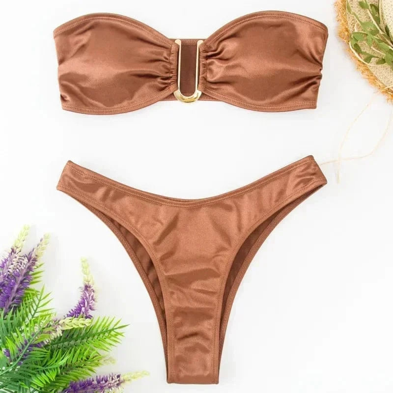 A metallic copper-toned two-piece bikini set featuring a strapless bandeau top with a gold-tone U-shaped center hardware accent and matching high-cut bikini bottoms arranged on a white surface with small floral accents.