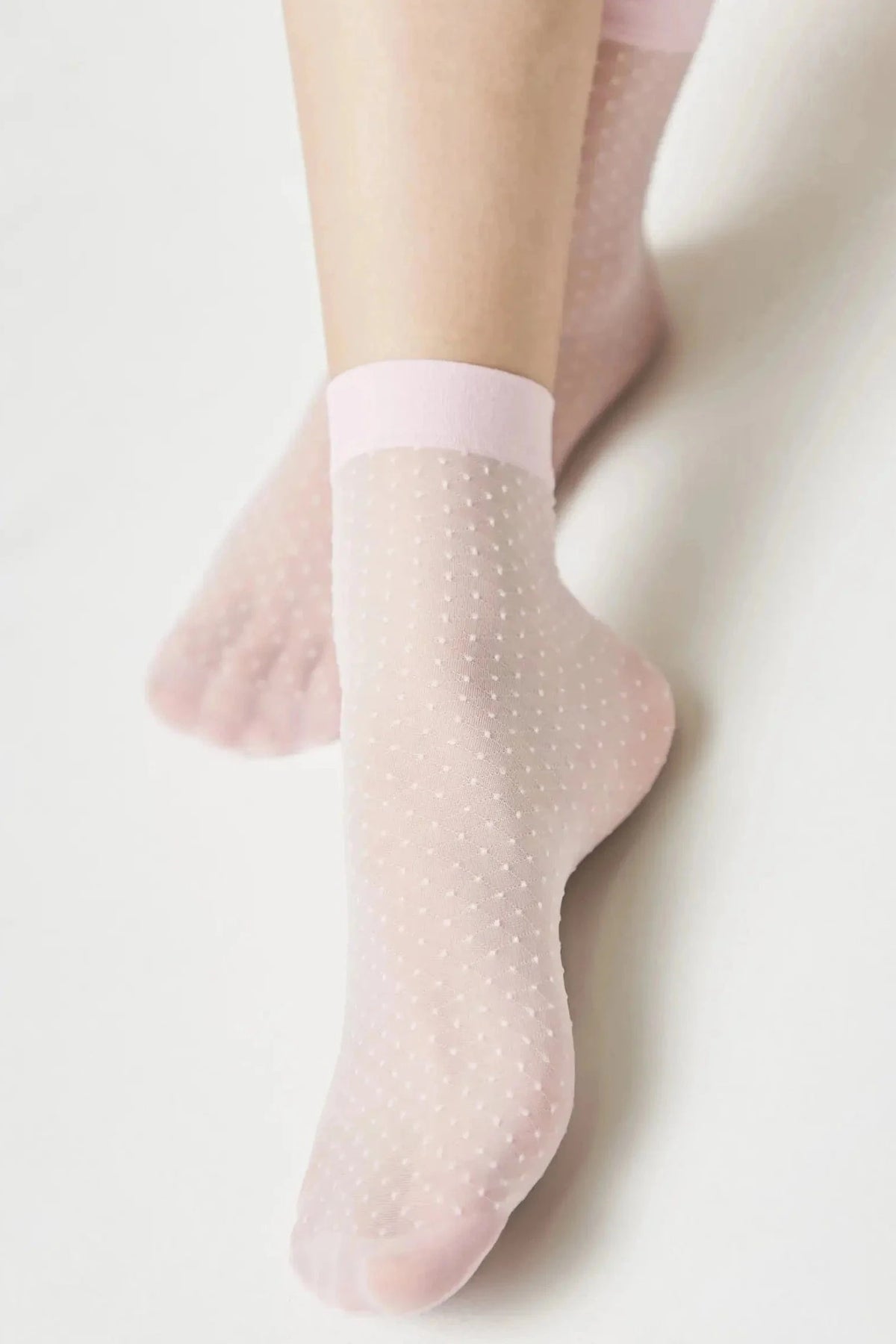 Sheer light pink ankle socks with a small white polka dot pattern and a solid pink cuff worn on a person's feet.