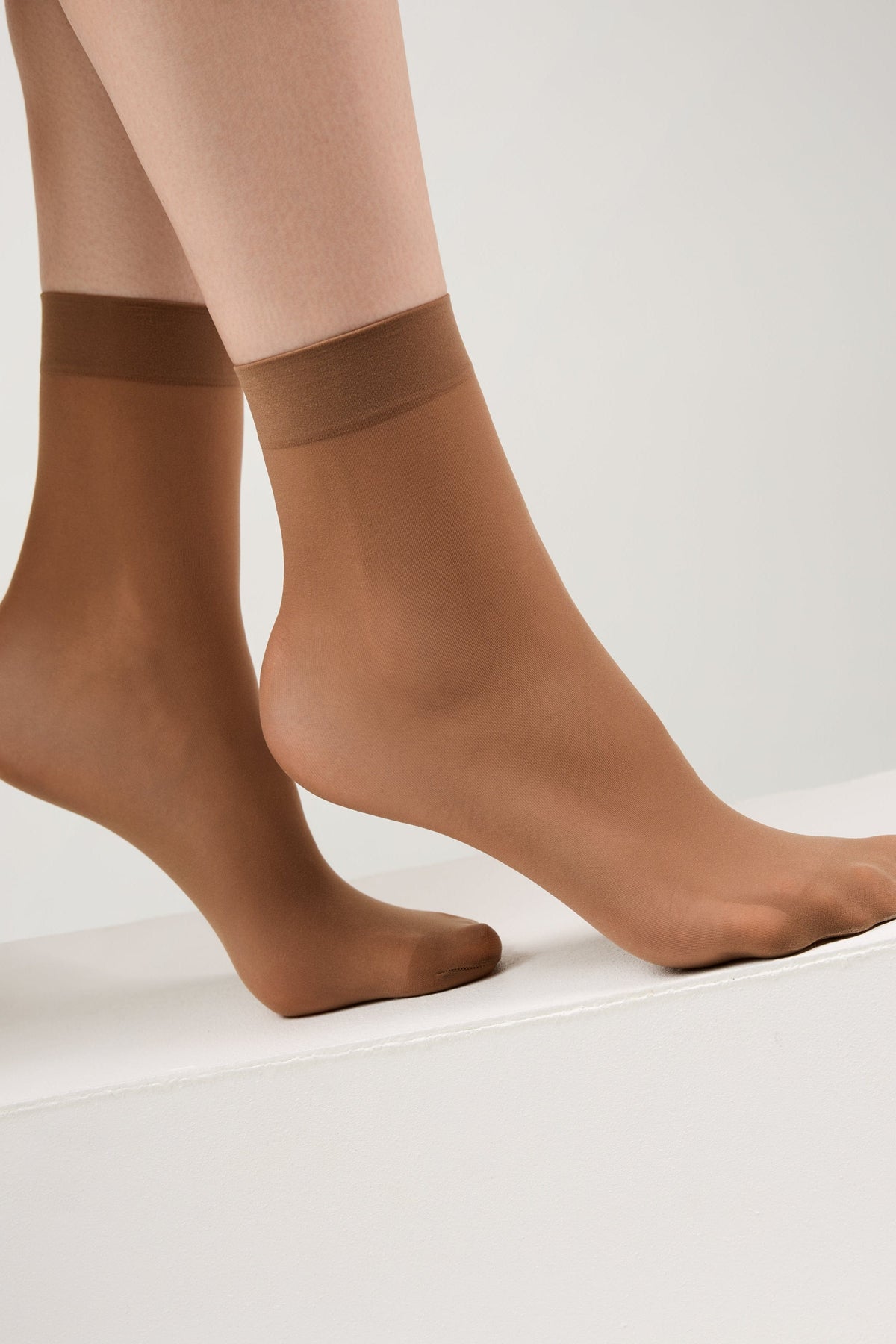A pair of sheer tan ankle-high hosiery socks shown on a person's feet against a white background.