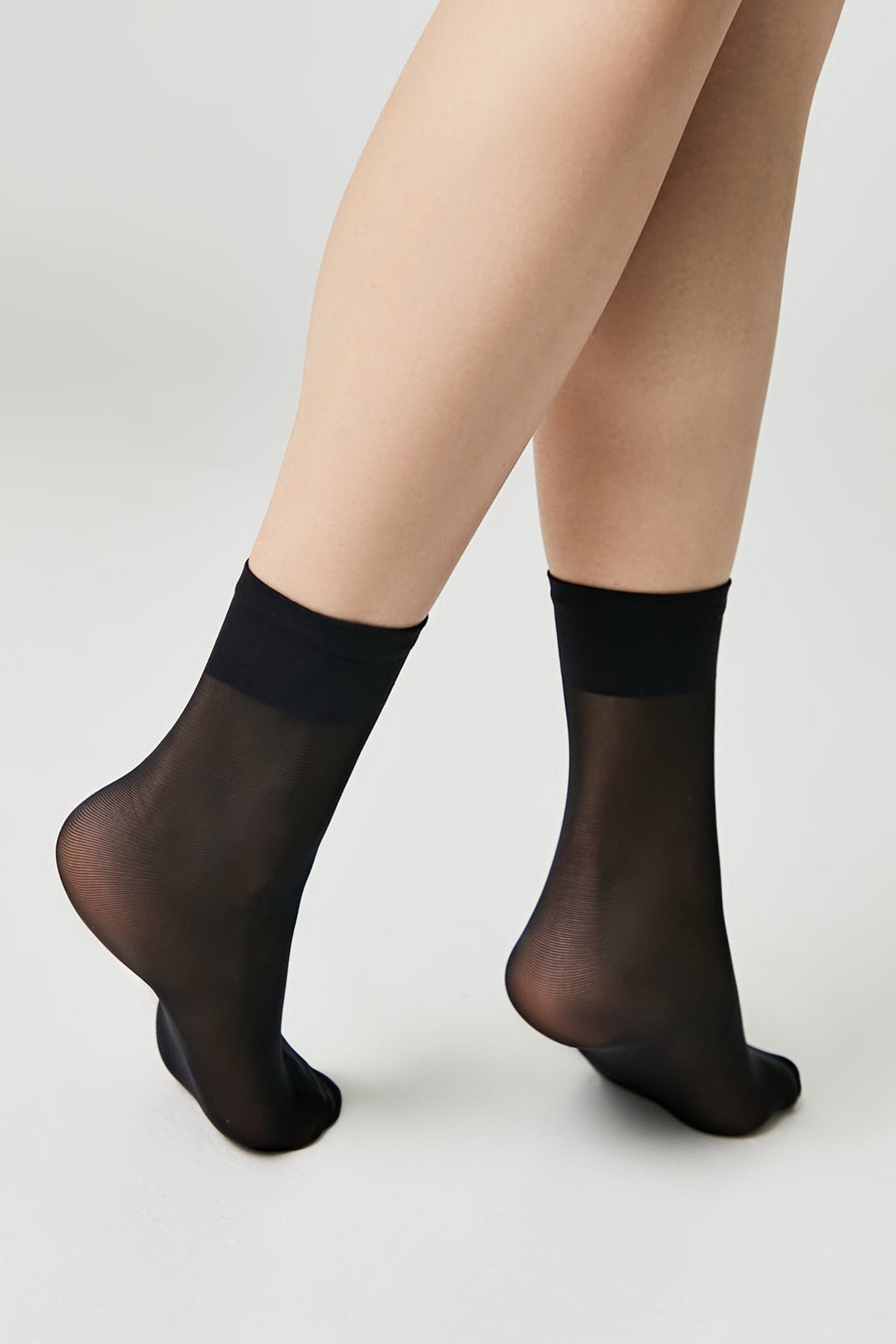Sheer black ankle socks worn on a pair of legs against a plain white background.