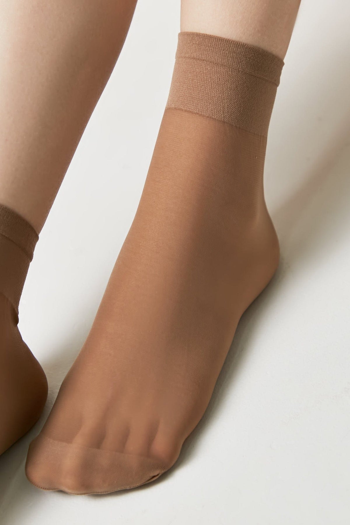 A pair of sheer tan ankle socks worn on a person's feet against a white background.