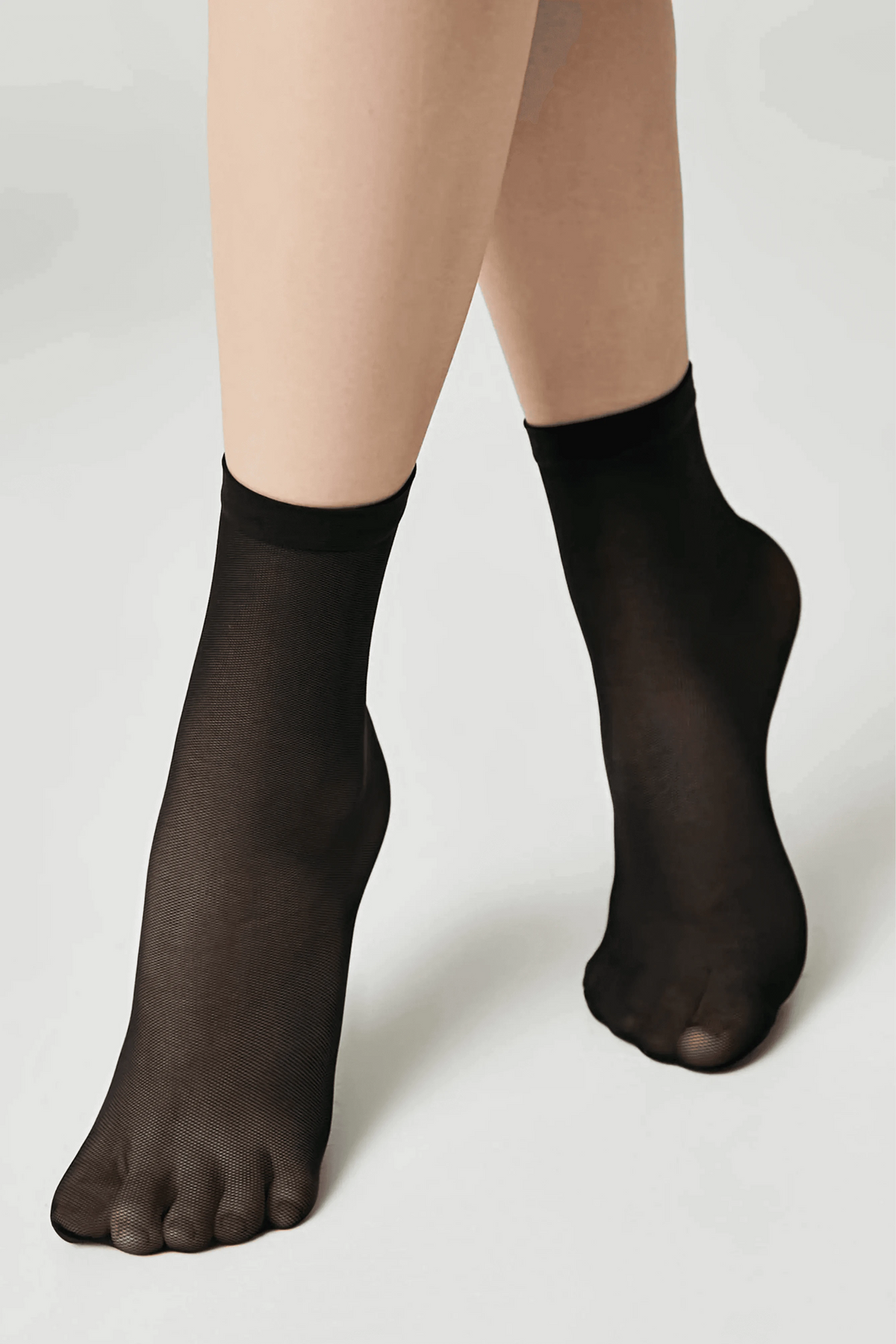 A pair of sheer black ankle socks worn on feet against a plain white background.