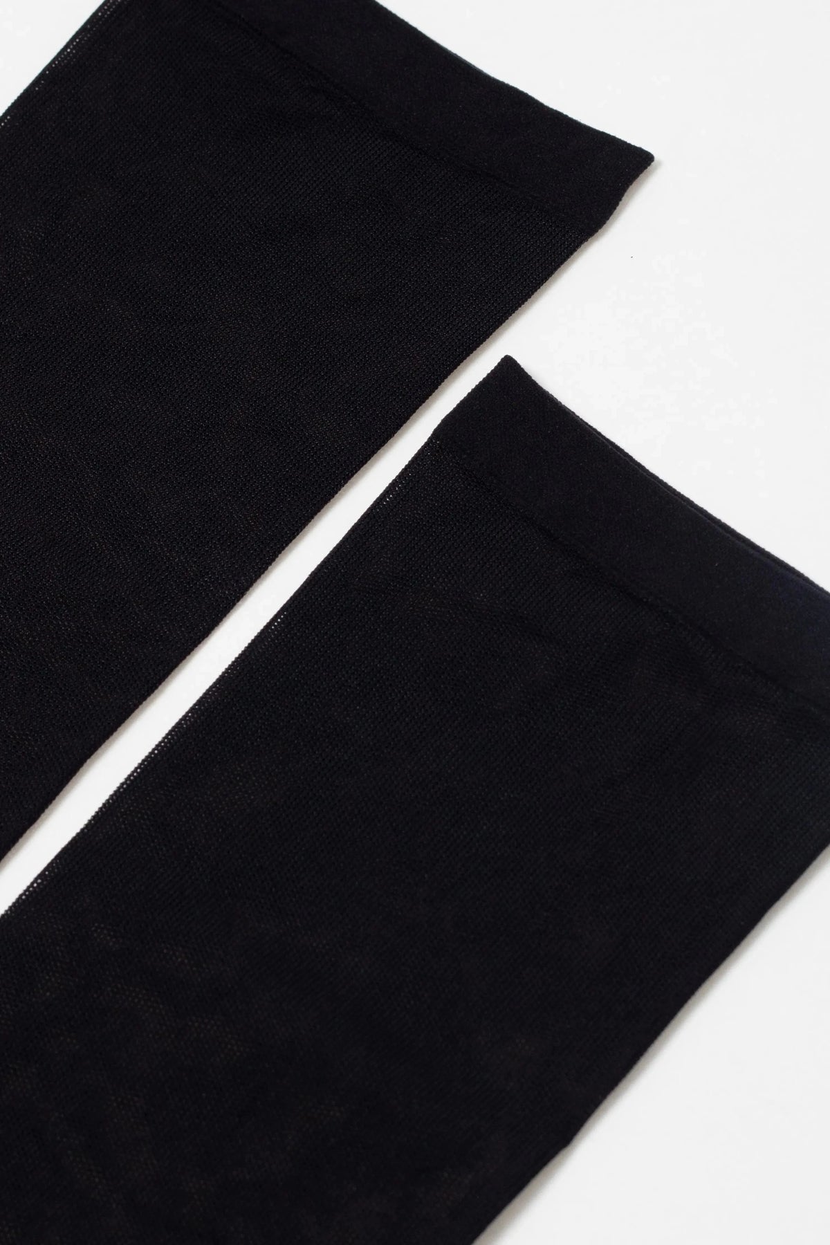 A pair of sheer black stockings laid flat against a plain white background.