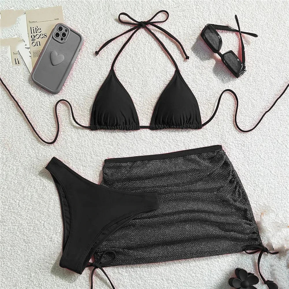 A black bikini set consisting of a triangle top and high-waisted bottom, paired with a matching sheer black mesh mini skirt, sunglasses, and a grey phone case against a white textured background.