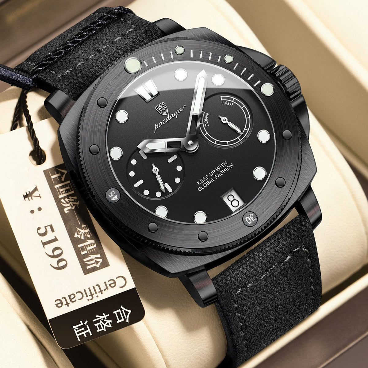 A black wristwatch with a round dial, sub-dials, and a date window sits inside a beige display box, accompanied by a small rectangular tag.