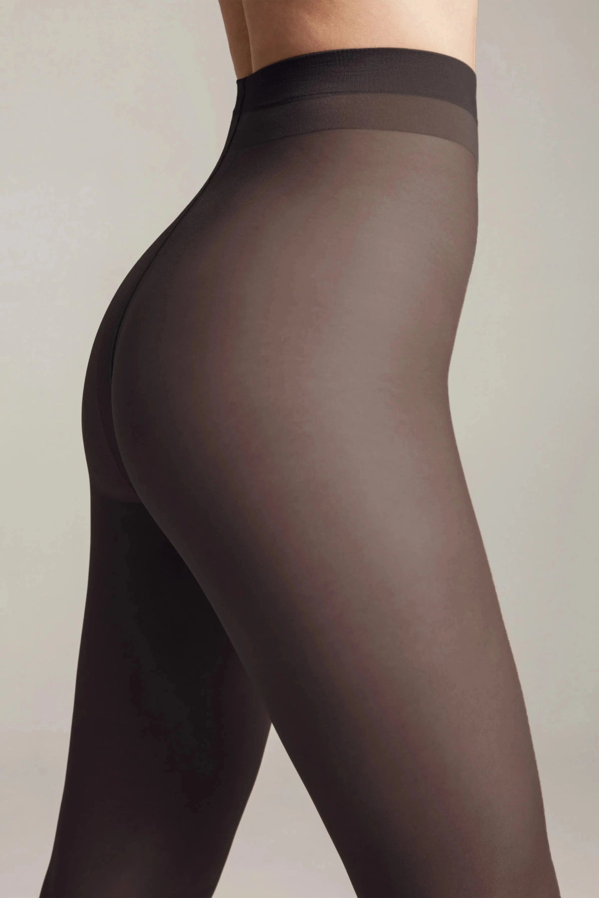 A close-up side profile view of a person wearing sheer black tights against a plain light gray background.