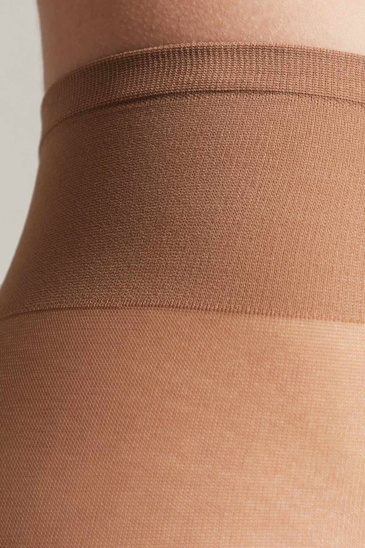 A close-up view of the waistband and upper leg portion of tan-colored sheer tights.