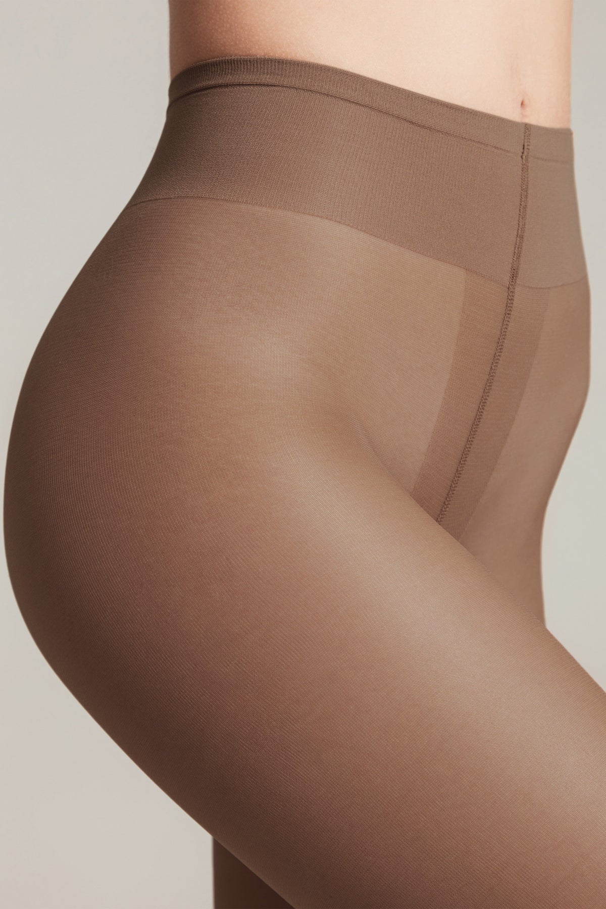 A close-up view of a person wearing sheer brown tights with a high-waisted, reinforced waistband.