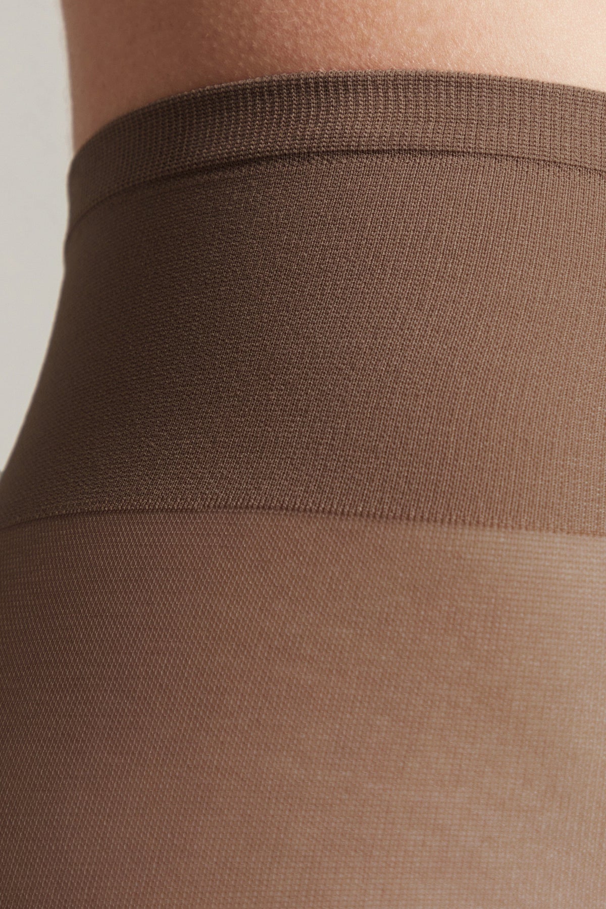 A close-up view of the waistband and top portion of brown nylon hosiery on a person's waist, showing the contrast between the darker elasticized band and the sheer fabric.