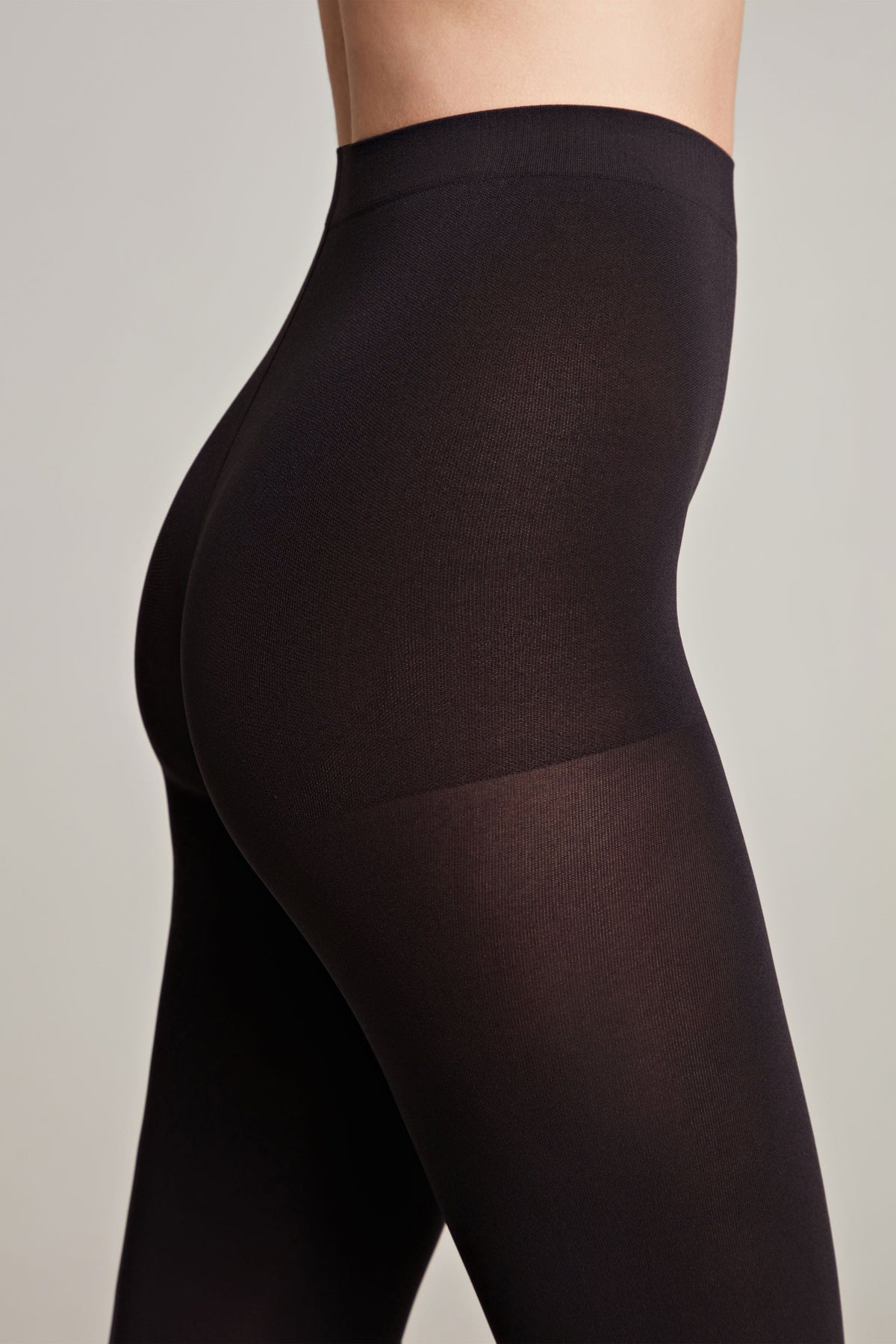 Black opaque tights worn by a person, shown from a side angle, featuring a seamless high-waist design.