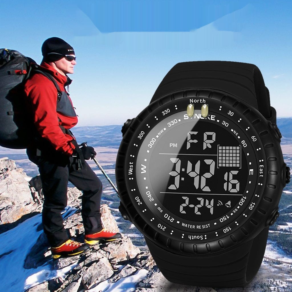 A black digital sports watch with a circular face is displayed against a background of a hiker standing on a snowy mountain peak.