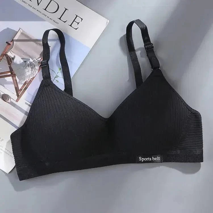 A black wireless bralette with adjustable shoulder straps and a small rectangular patch labeled Sports belt on the bottom band, displayed against a neutral background next to a magazine.
